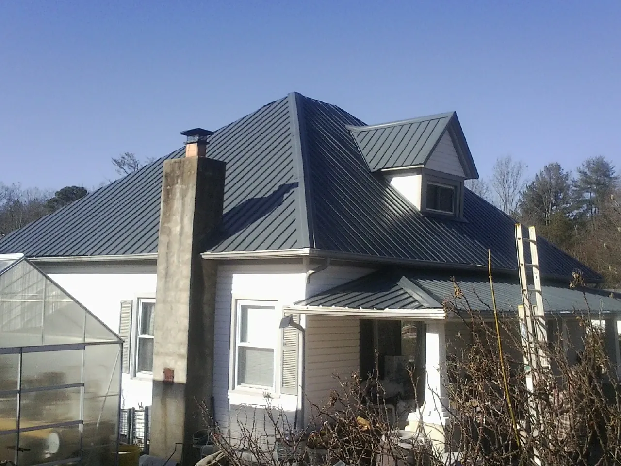 Dark blue standing seam metal roof on a white farmhouse with dormer — Slate & Tile Roof Repair by Roofing Brothers in Minetto