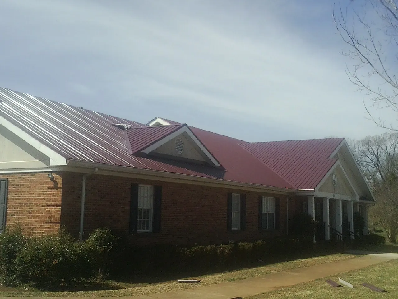 Red metal roof with gabled entries on a long brick building, from a Hail Damage Roof Repair job in Minetto