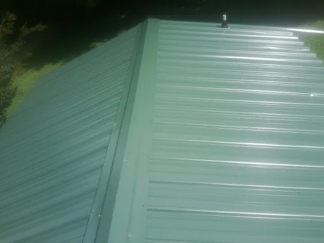New green metal panels meeting at the ridge of a roof — Flat Roof Repair work by our crew in Minetto