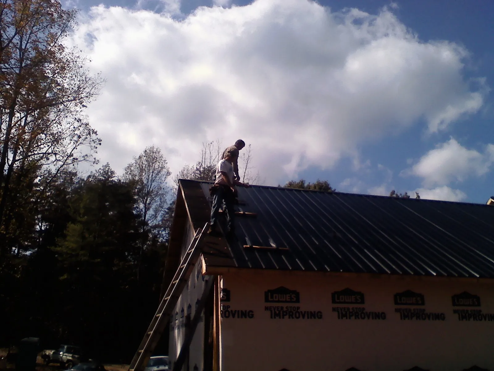 Roofer fastening dark metal panels high against a cloudy sky, from a Roof Inspection job in Minetto