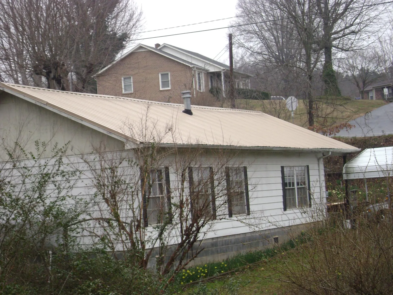 Tan metal roof on a white sided house set into a hillside — Commercial Roofing by Roofing Brothers in Minetto