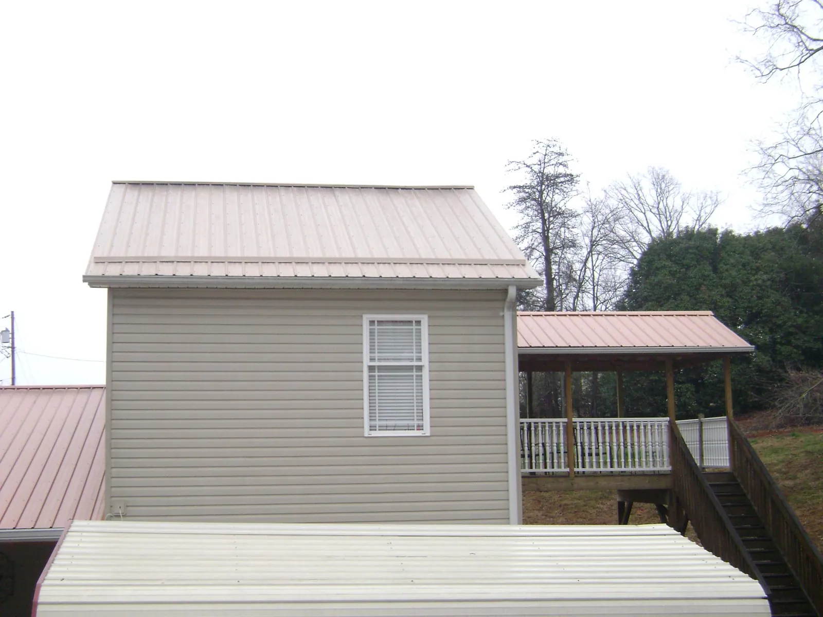 Tan metal roofs on a two story addition and attached porch, from a Roof Replacement job in Minetto